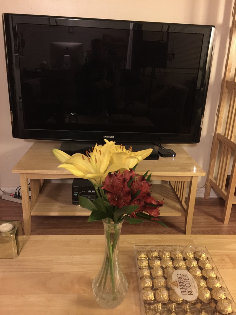 yellow lilies and red alstromeria beside a box of chocolates 